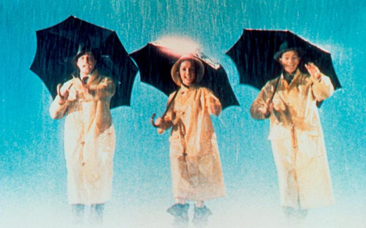 three actors with umbrellas and raincoats singing in the rain